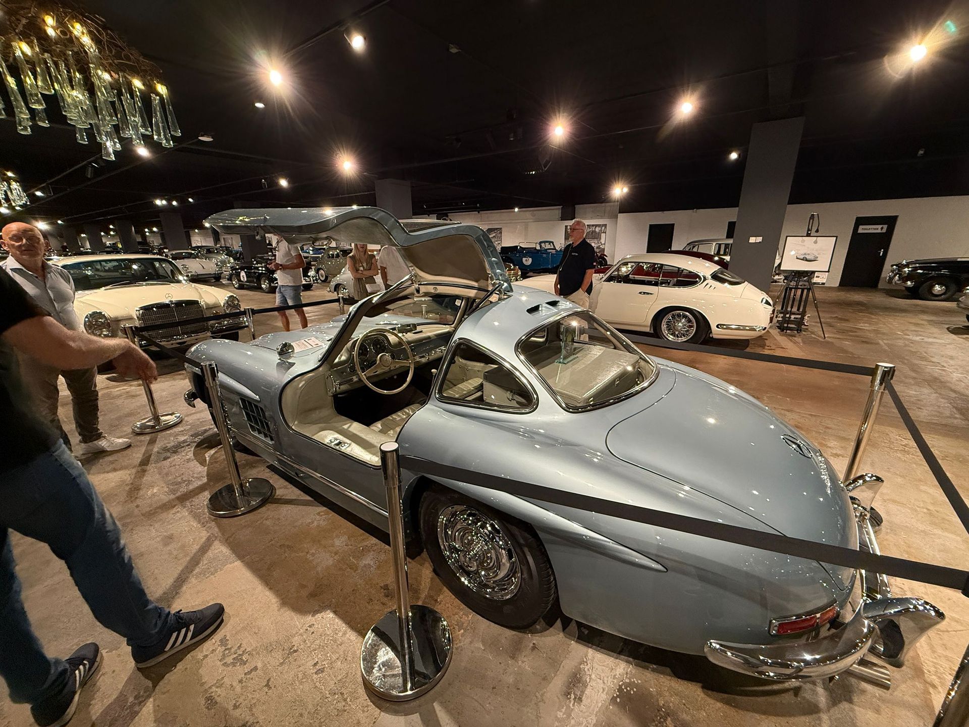 Lichtblauwe Mercedes-Benz 300SL Gullwing coupé, met open vleugeldeuren, tentoongesteld in een museum.