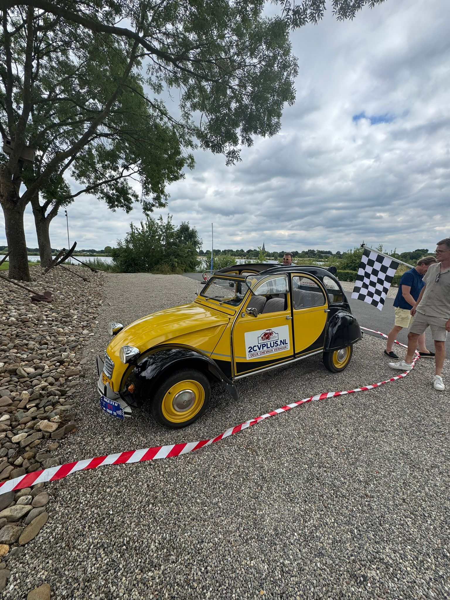 Een geel-zwart speelgoedautootje op een buitenevenement, met een geblokte vlag en toeschouwers.