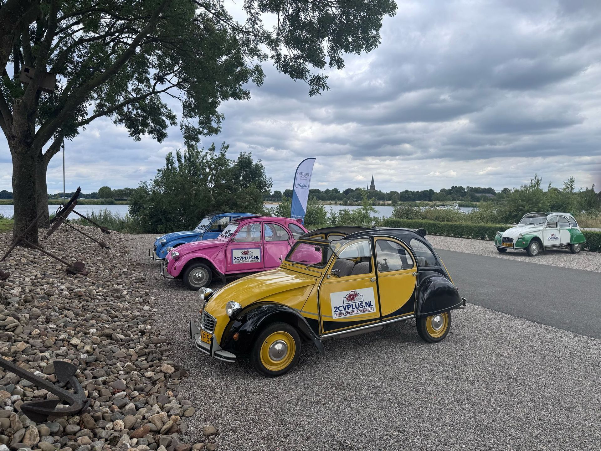 Drie kleurrijke Citroën 2CV's geparkeerd aan de rand van een waterpartij.