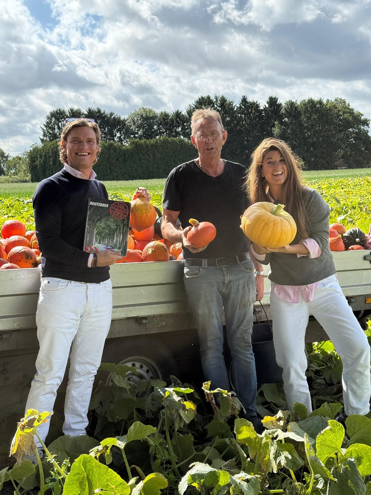 Drie mensen met pompoenen in hun handen staan in een veld met een pompoenententoonstelling.