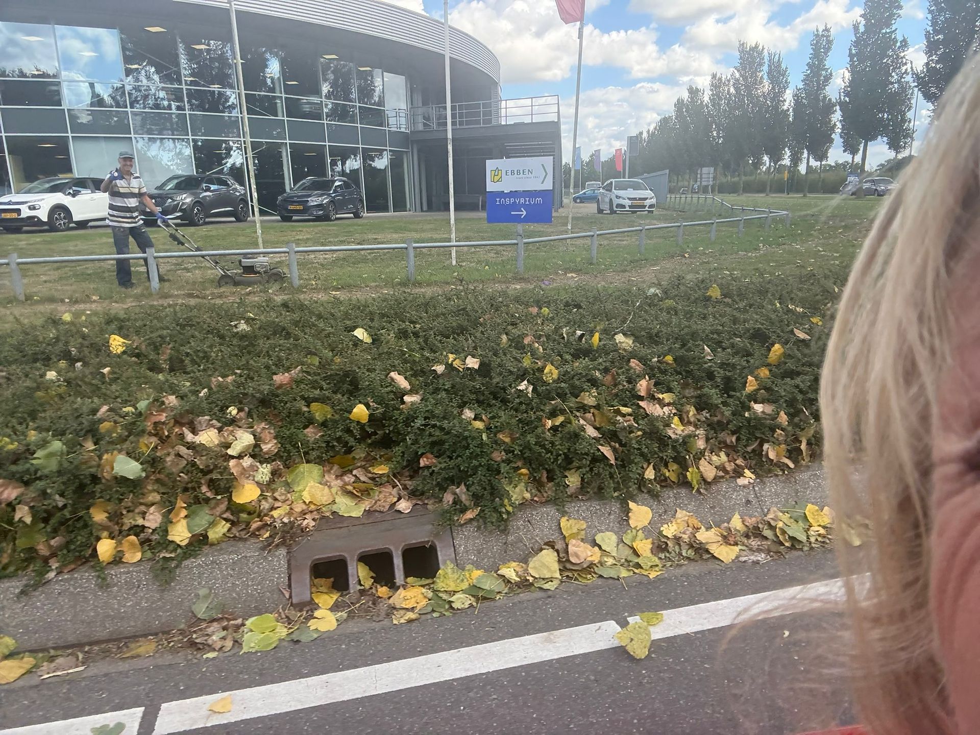 Een gazon met bladeren voor een gebouw; rechts is een persoon zichtbaar.