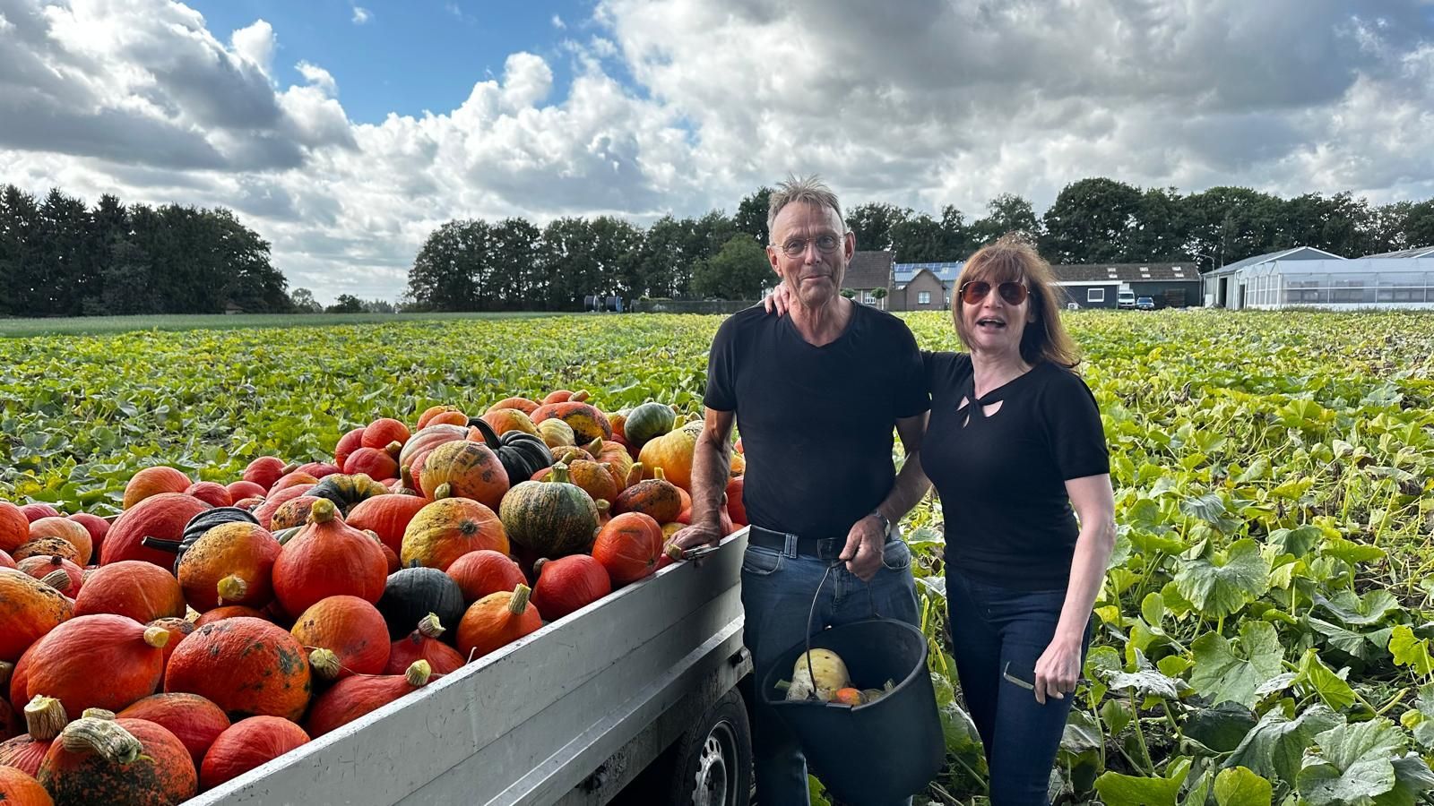 Een stel staat naast een vrachtwagen vol pompoenen in een veld, onder een bewolkte hemel.