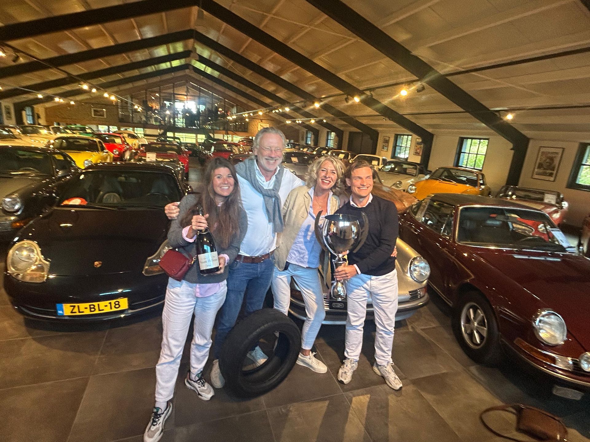 Groepsfoto's met auto's, een trofee en een band in een grote showroom. Vrolijke gezichten, lichte omgeving.