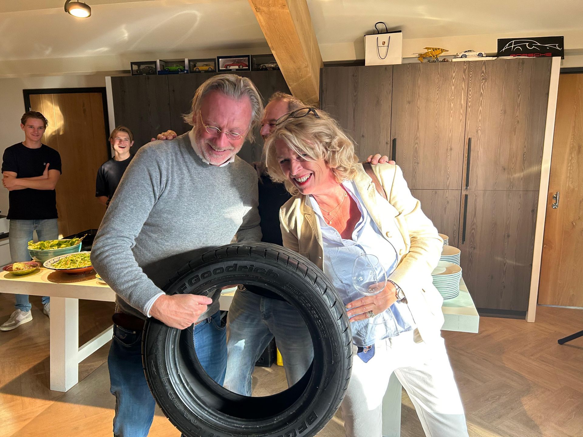Drie mensen glimlachen terwijl ze een autoband vasthouden. Een man links en een vrouw rechts. Nog iemand staat erachter. Een lichte ruimte.