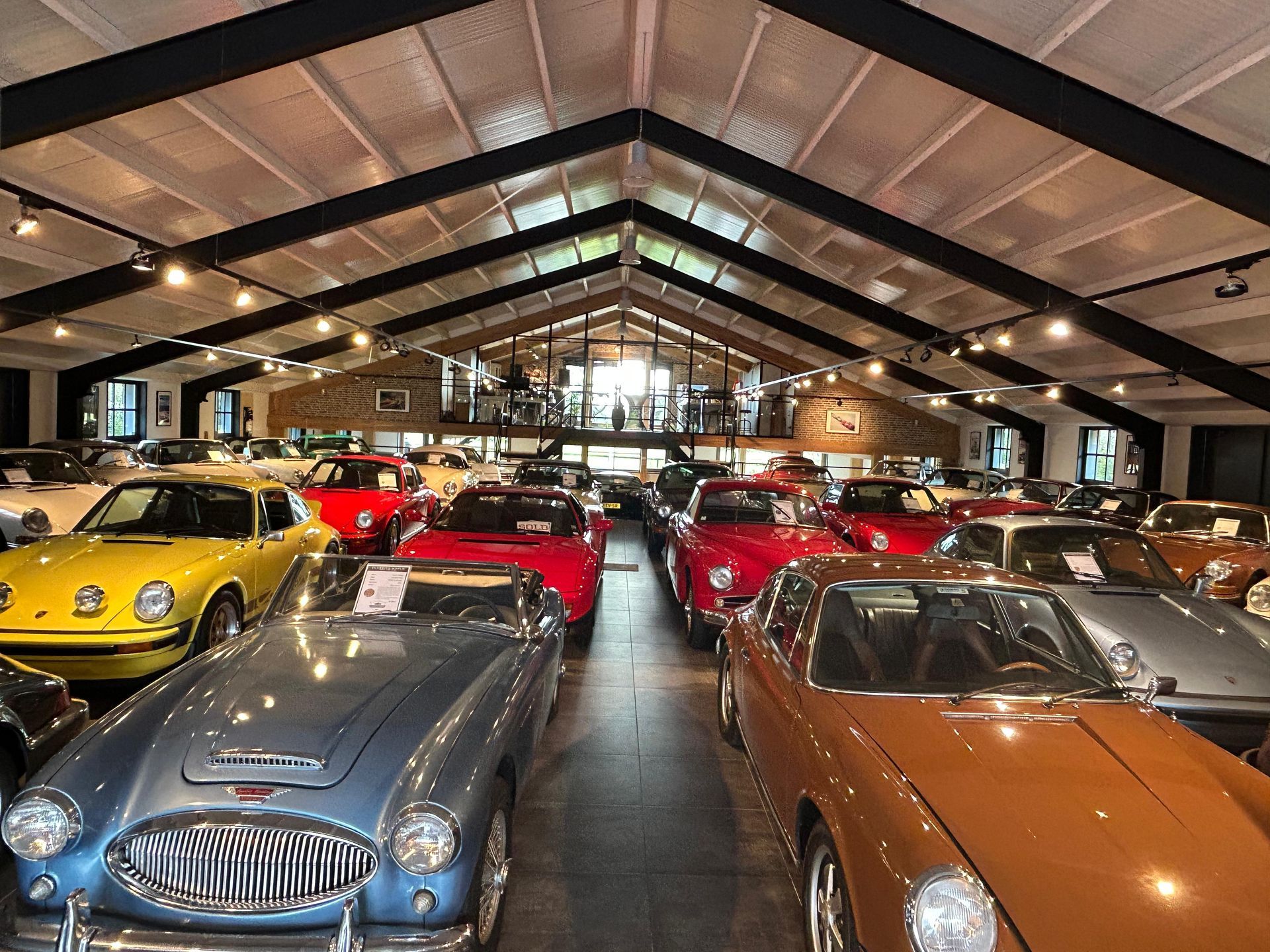 Klassieke auto's tentoongesteld in een grote, lichte showroom. Diverse kleuren, waaronder rood, blauw en geel.