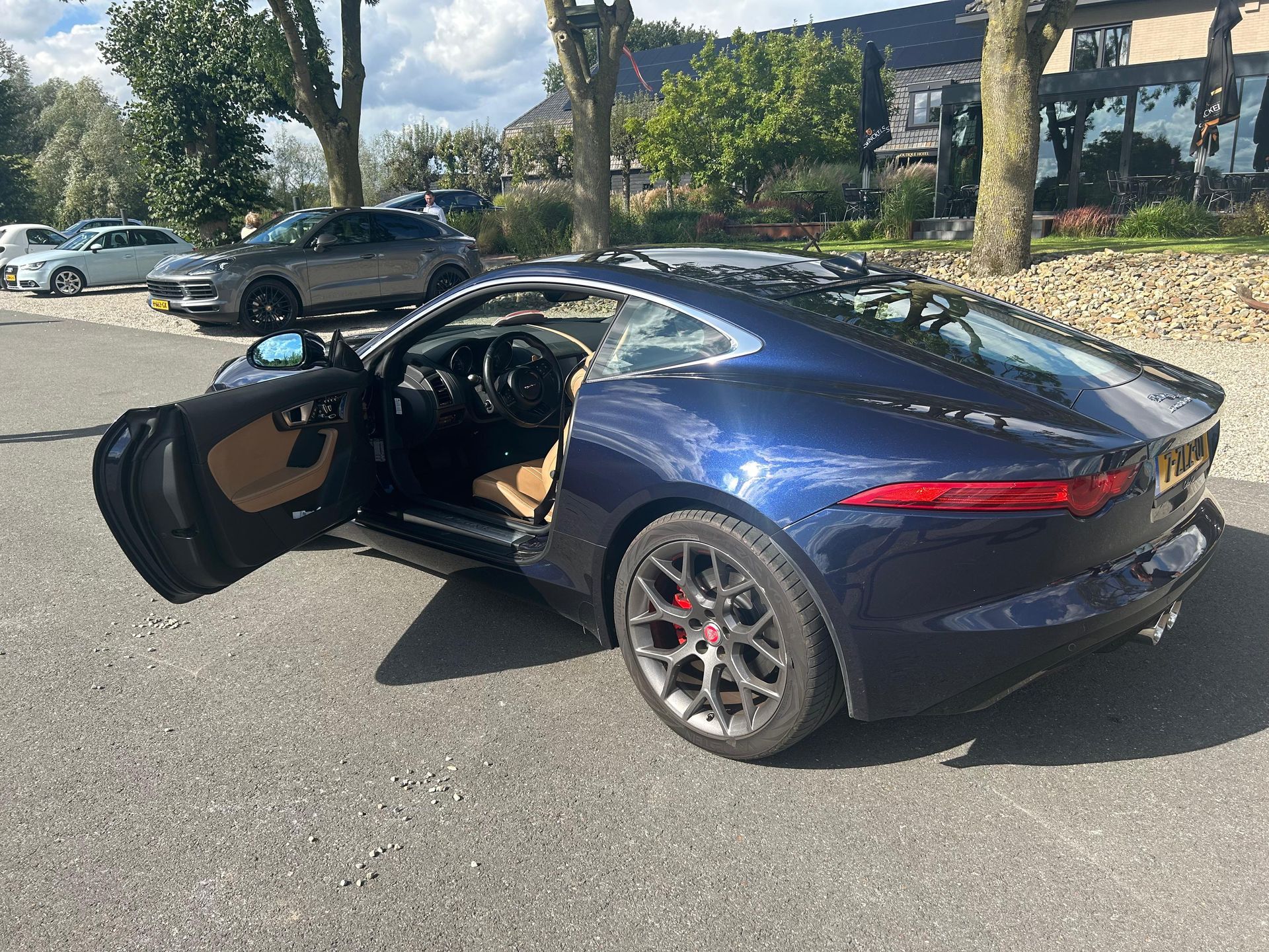Blauwe Jaguar sportwagen met open deur, geparkeerd op een verharde parkeerplaats.