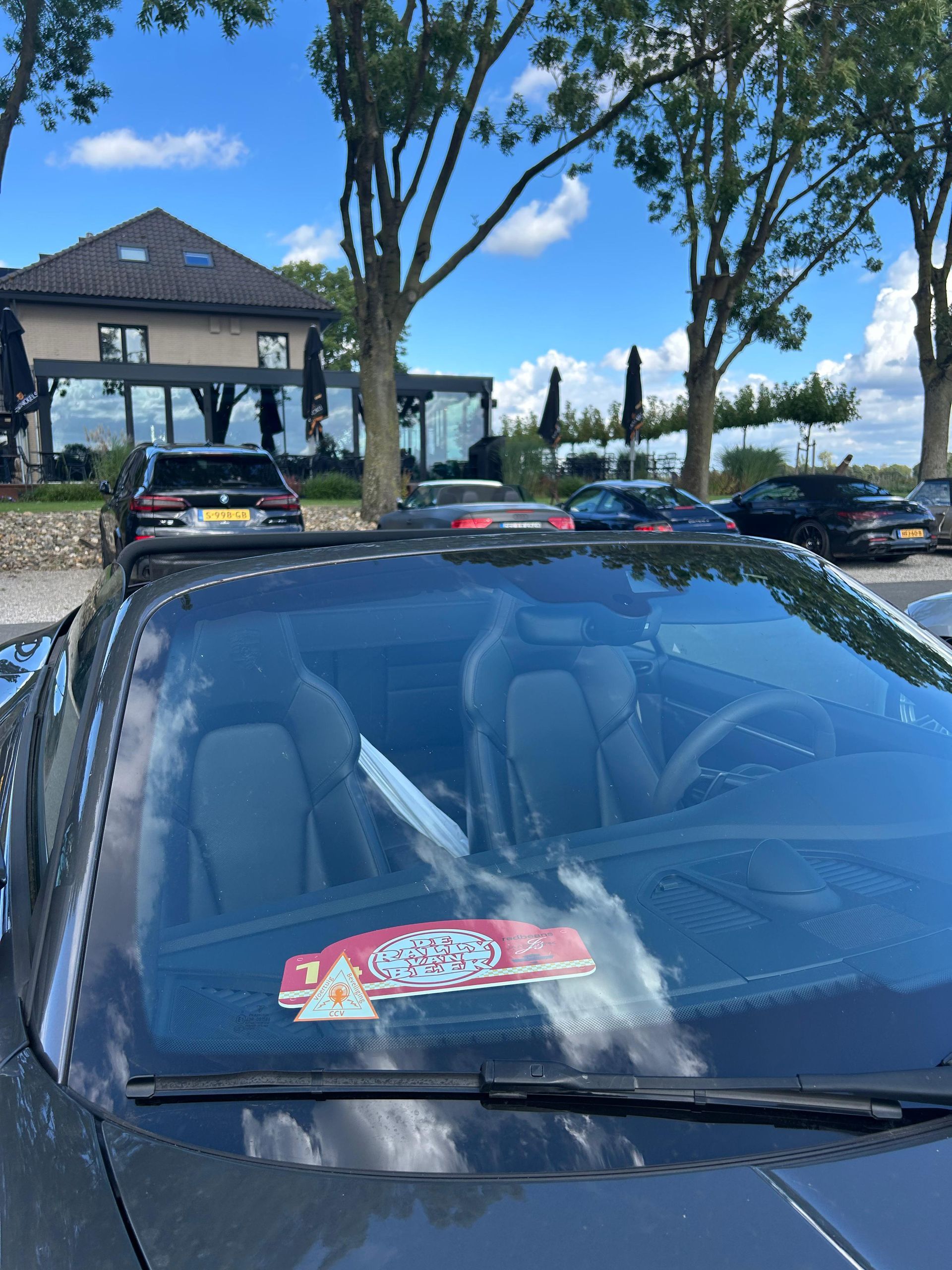 Auto's geparkeerd voor een gebouw met bomen en een blauwe lucht.