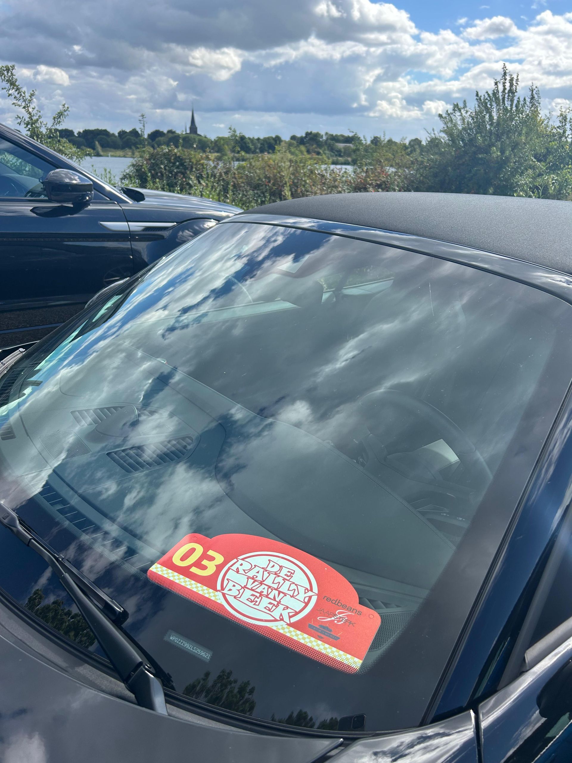 Voorruit van een cabriolet met een rode parkeervergunning, bewolkte lucht op de achtergrond.