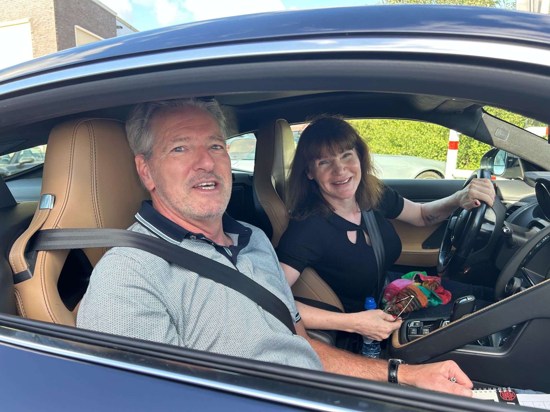 Man en vrouw in een blauwe auto. De vrouw bestuurt de auto. Beiden glimlachen. Beige interieur.