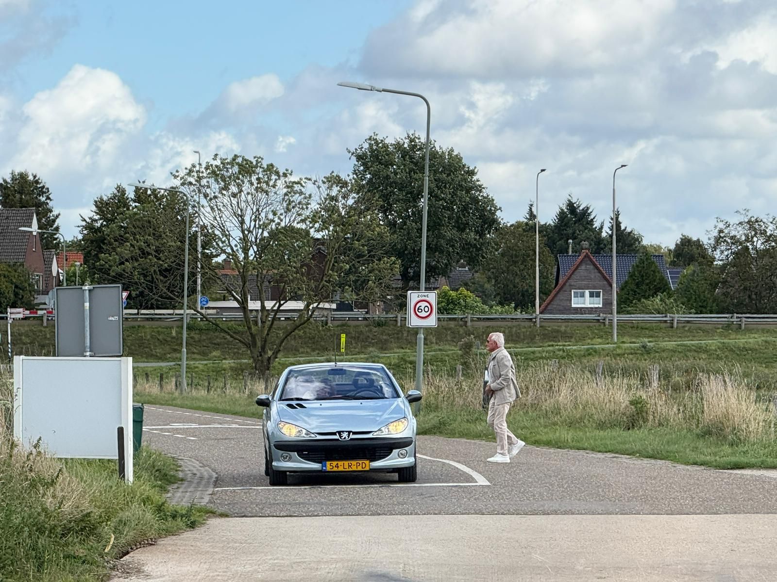 Een auto nadert een voetganger bij een zebrapad in een landelijke omgeving op een zonnige dag.