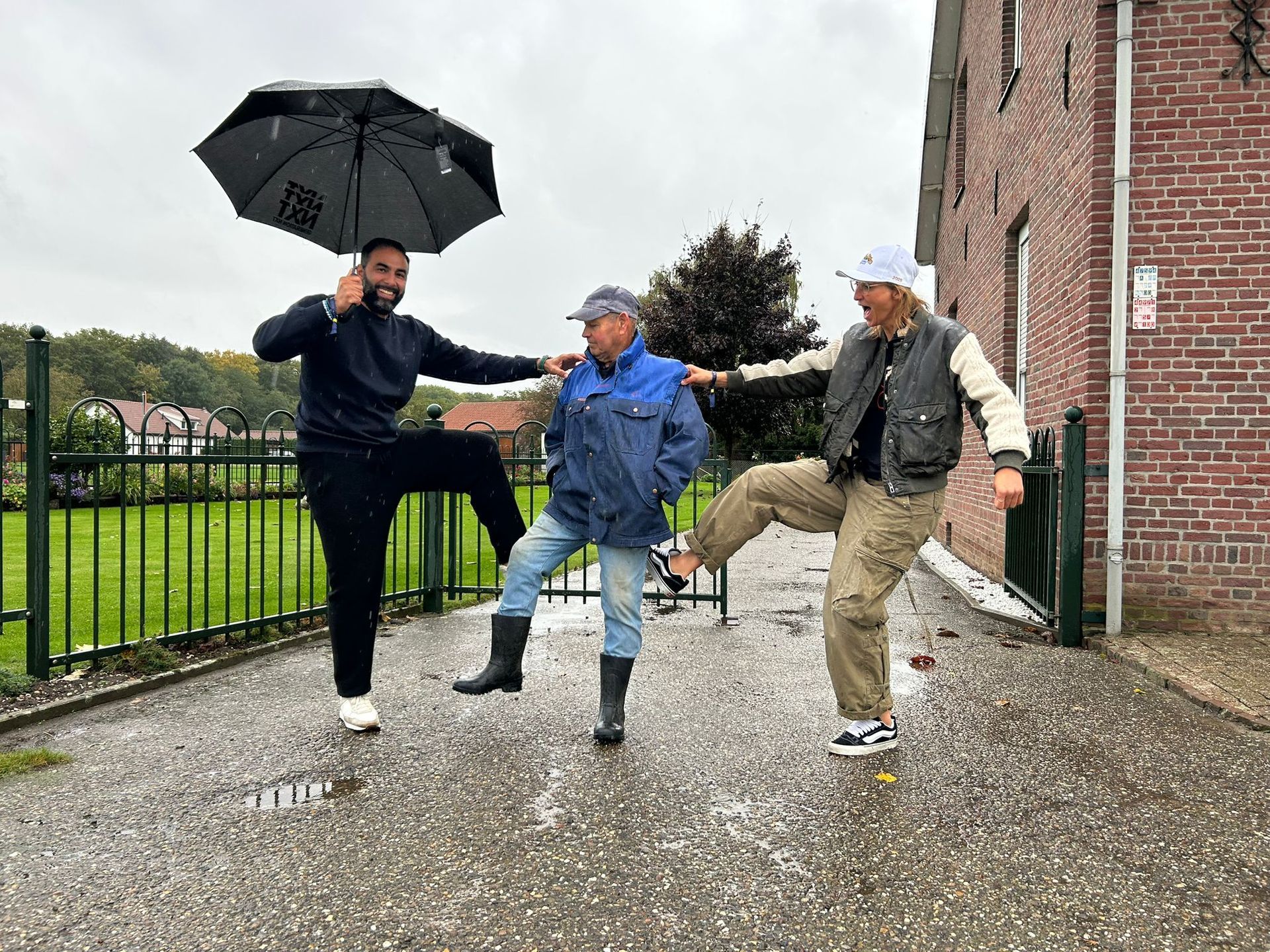 Drie mensen schoppen met hun benen in de regen, één van hen houdt een paraplu vast.