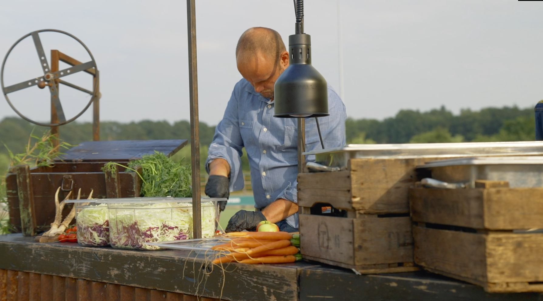Man in blauw shirt bereidt eten bij een kraam buiten en snijdt groenten.
