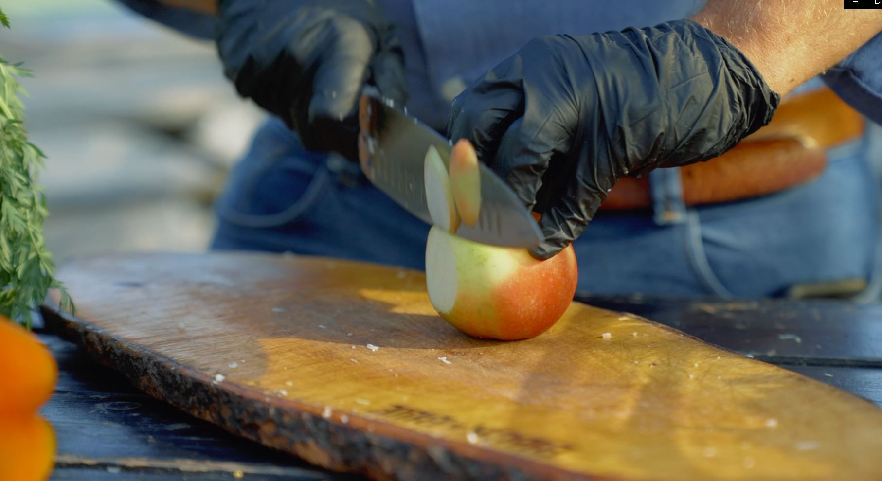 Een persoon met zwarte handschoenen snijdt een appel op een houten plank.