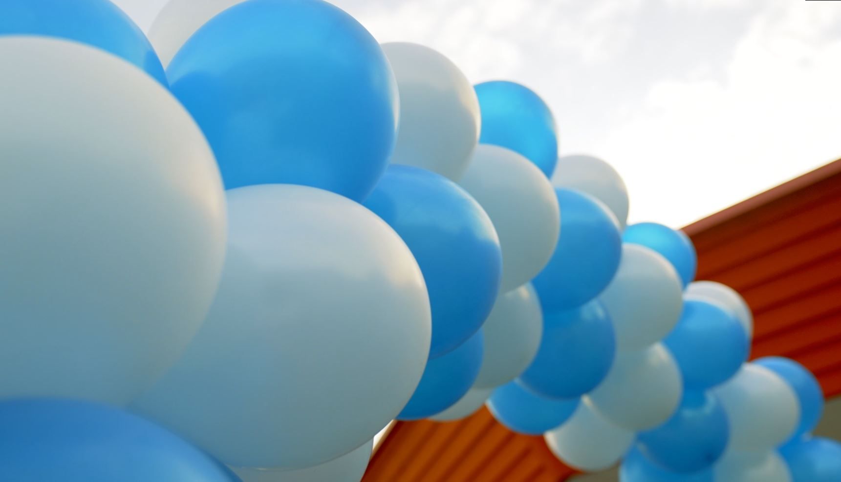 Blauwe en witte ballonnen vormen een boog, waarschijnlijk voor een feest, voor een rood gebouw.