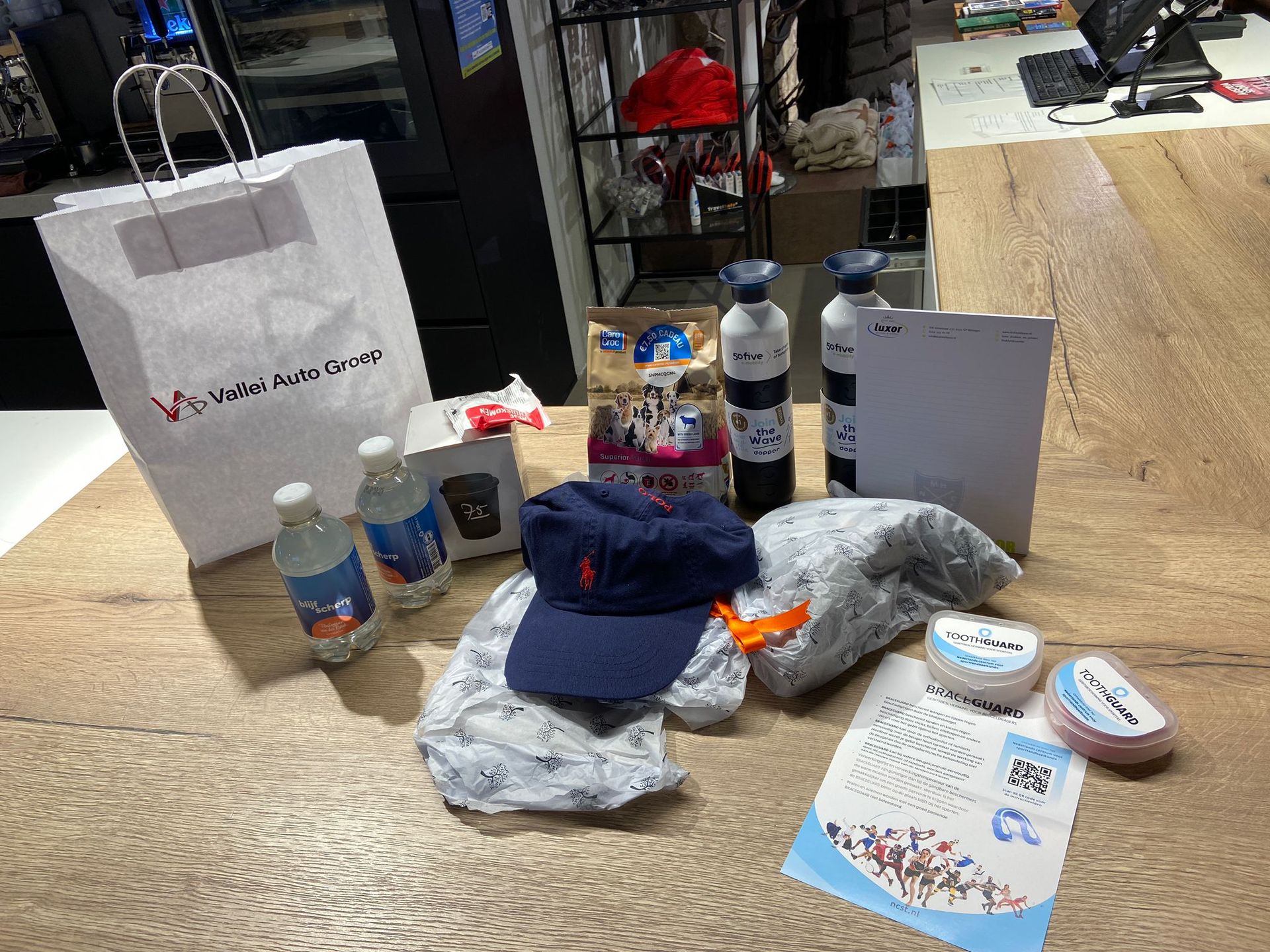 Een tafel met cadeautjes, waaronder een tas, waterflessen, een pet en snacks.