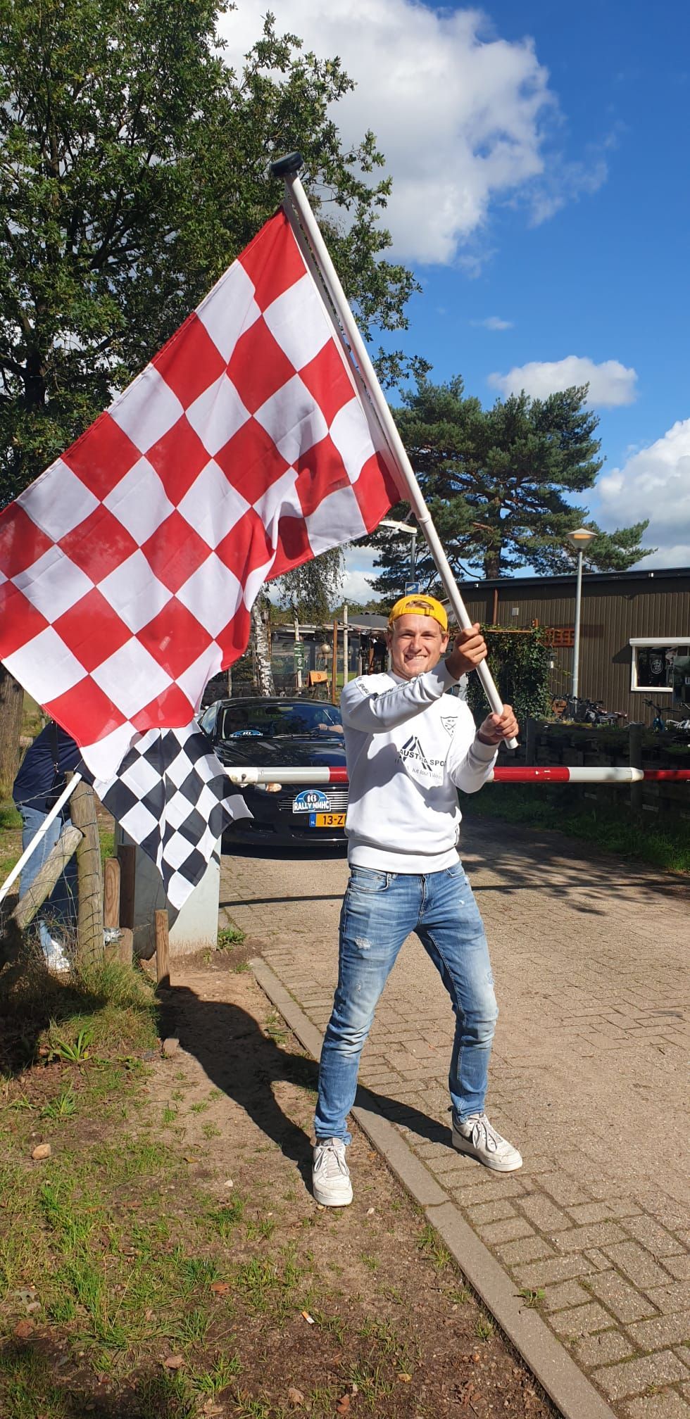 Een persoon met een grote rood-wit geblokte vlag staat buiten. Een kleinere geblokte vlag is ook zichtbaar.