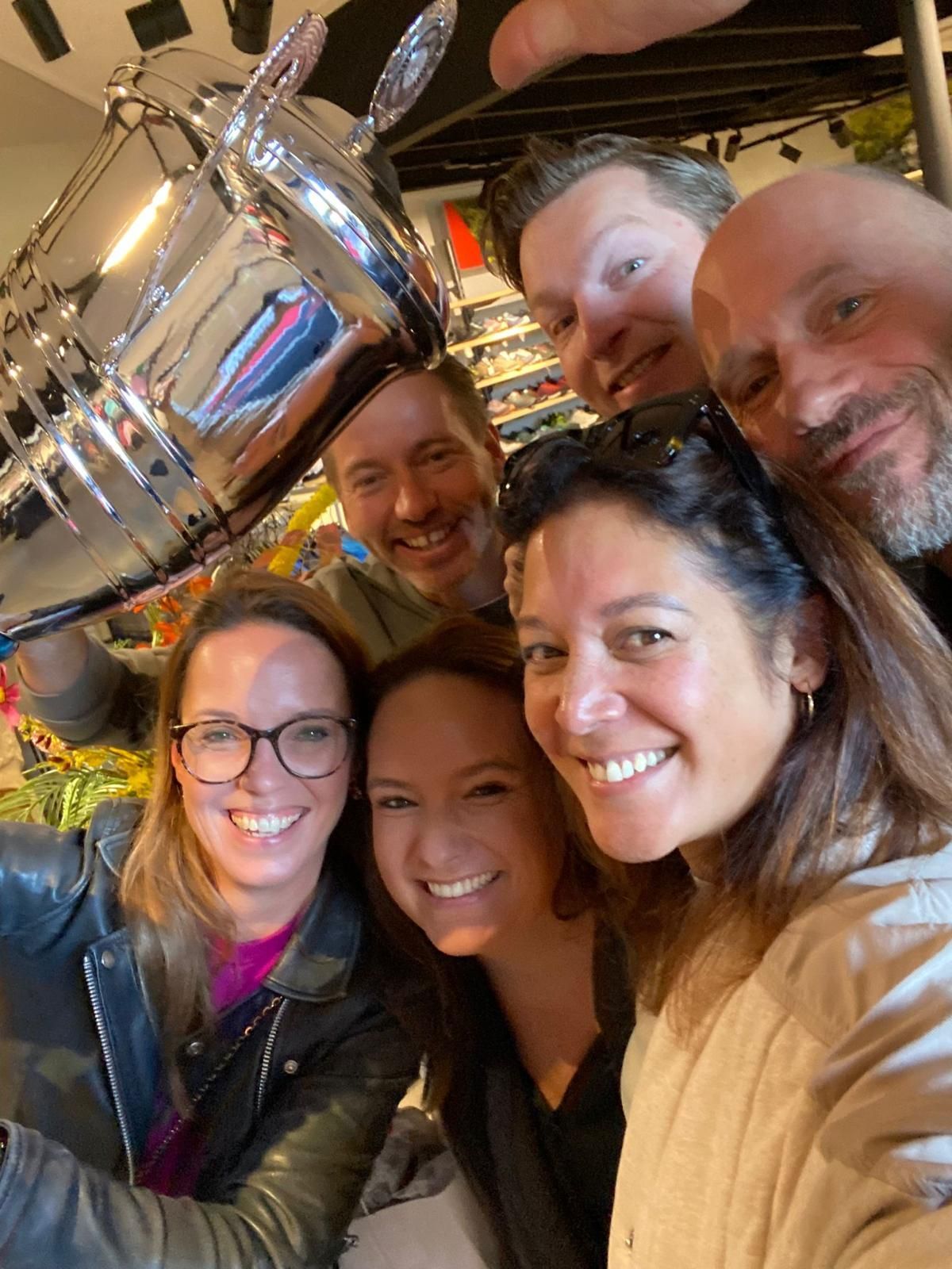 Groepsfoto, lachend, met een zilveren trofee in de hand in een winkel.