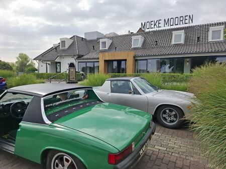 Twee klassieke Porsche 914's staan ​​geparkeerd voor een gebouw genaamd 