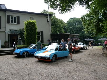 Klassieke sportauto's staan ​​geparkeerd voor een gebouw; mensen verzamelen zich in de buurt.