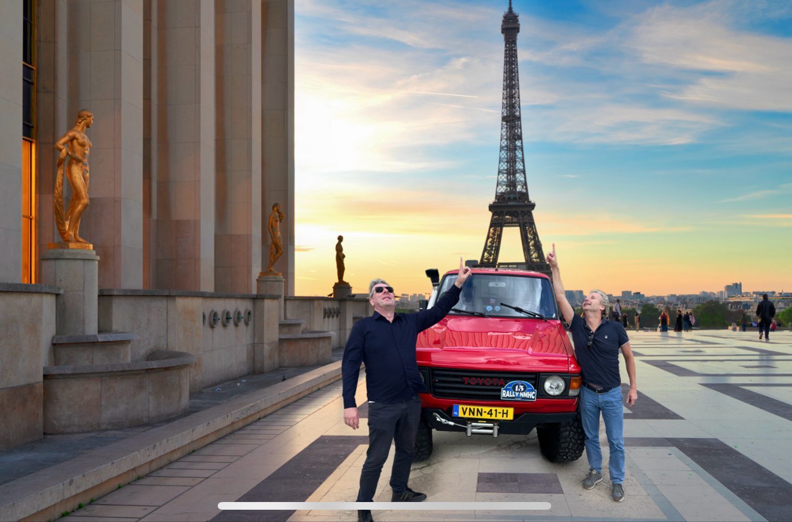 Twee mannen poseren naast een rode SUV met de Eiffeltoren op de achtergrond. Ook de zonsondergang, beelden en een geplaveid gebied zijn zichtbaar.