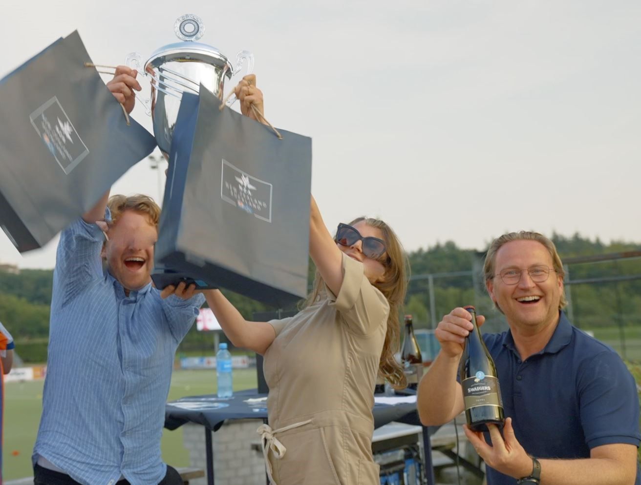 Mensen vieren feest, met trofeeën, tassen en flessen in hun handen. Ze lachen en zijn opgewonden.