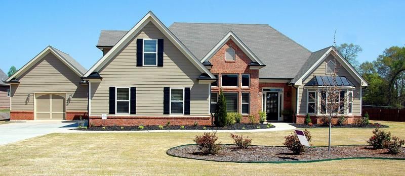 Single-story suburban house with tan siding, brick accents, and a manicured front yard