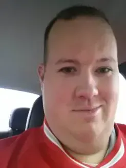Person in a red jacket smiling inside a car.