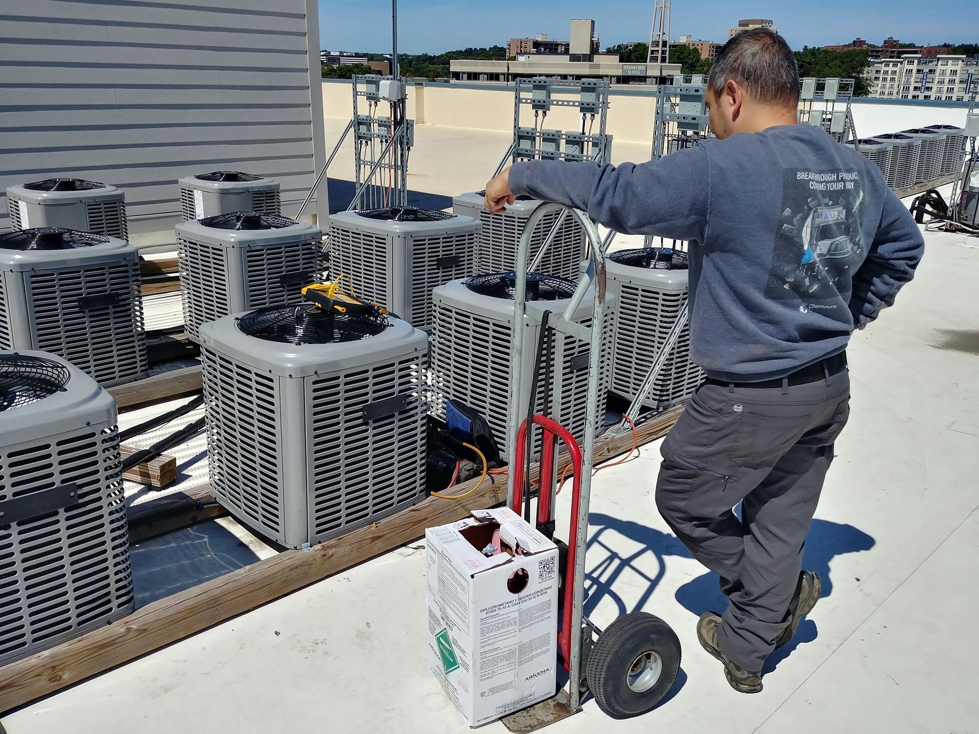 A man is standing on a roof next to a box of refrigerant.