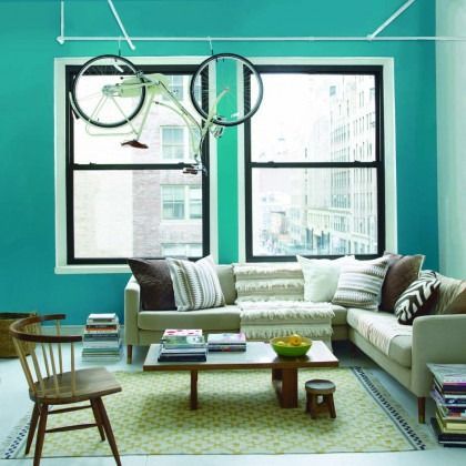 Bright turquoise living room with white sectional sofa, coffee table, chair, and large windows with hanging bicycles