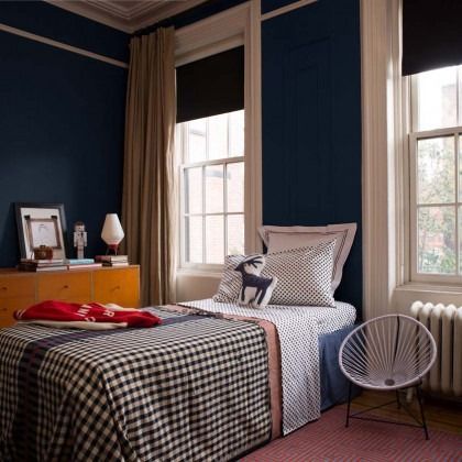 Cozy bedroom with navy walls, checkered bedspread, and a chair by the window