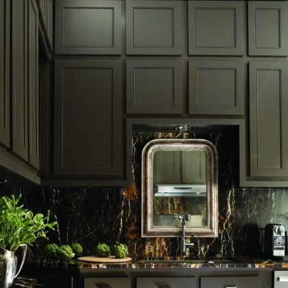 Dark modern kitchen with black cabinets, marble backsplash, and a stainless sink under a window.