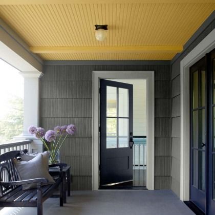 Covered porch with black chairs, purple flowers, gray siding, and a blue door leading inside
