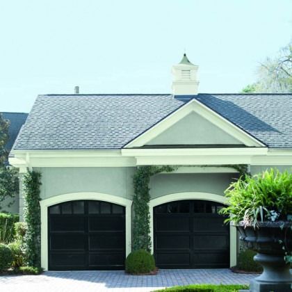 Two-car garage with dark doors, gray shingled roof, and white trim on a house facade