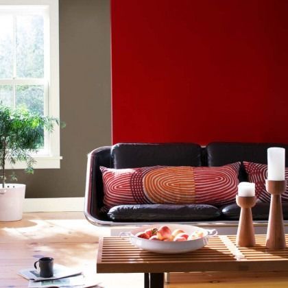 Modern living room with red accent wall, black sofa, wooden coffee table, and window light