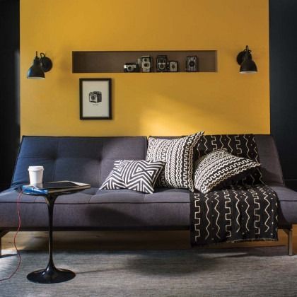 Modern living room with yellow accent wall, dark sofa, patterned pillows, and a small side table