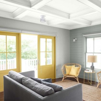 Bright living room with gray sofa, yellow French doors, wicker chair, and lamp by the window