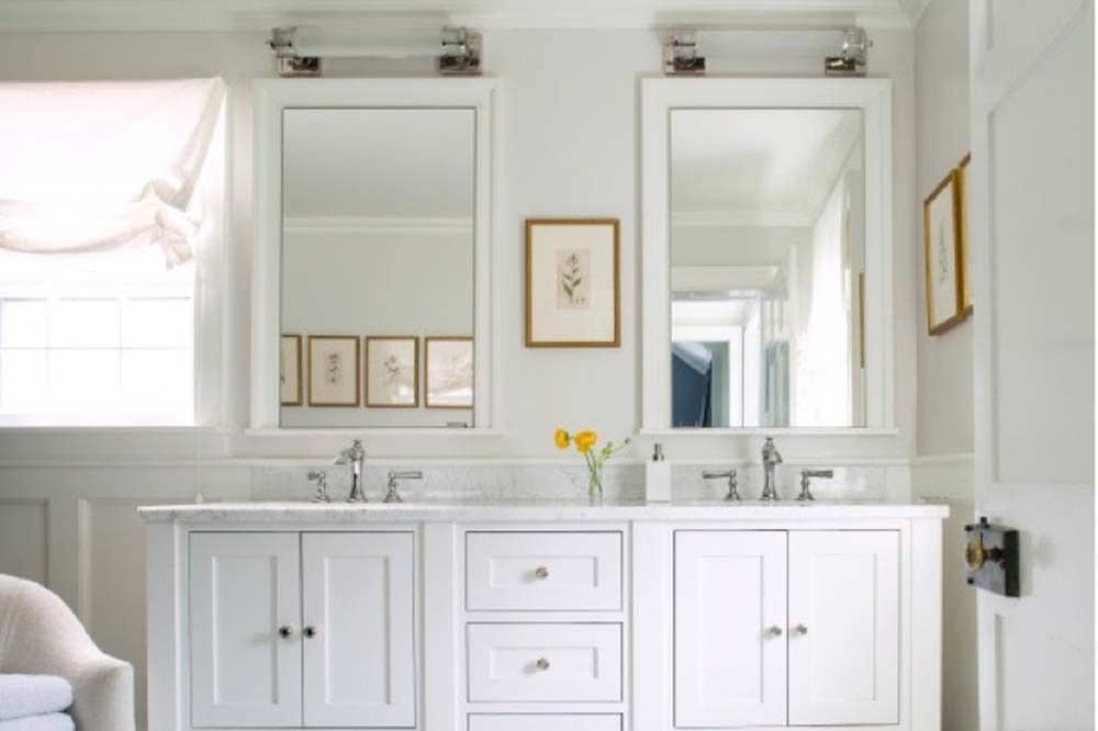 Bright white bathroom with double vanity, twin mirrors, and soft pink window curtains
