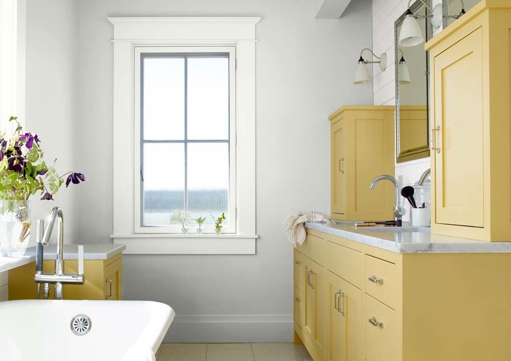 Bright bathroom with yellow cabinetry, white tub, and window with flowers on the sill