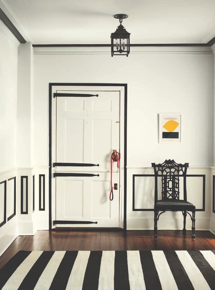 Minimalist hallway with a white door, black trim, chair, wall art, and striped rug