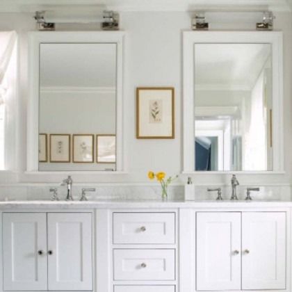 Bright white bathroom vanity with two mirrors, chrome faucets, framed art, and a small yellow flower vase.