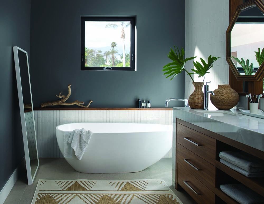 Modern bathroom with a freestanding tub, dark walls, wood vanity, and plants by the window