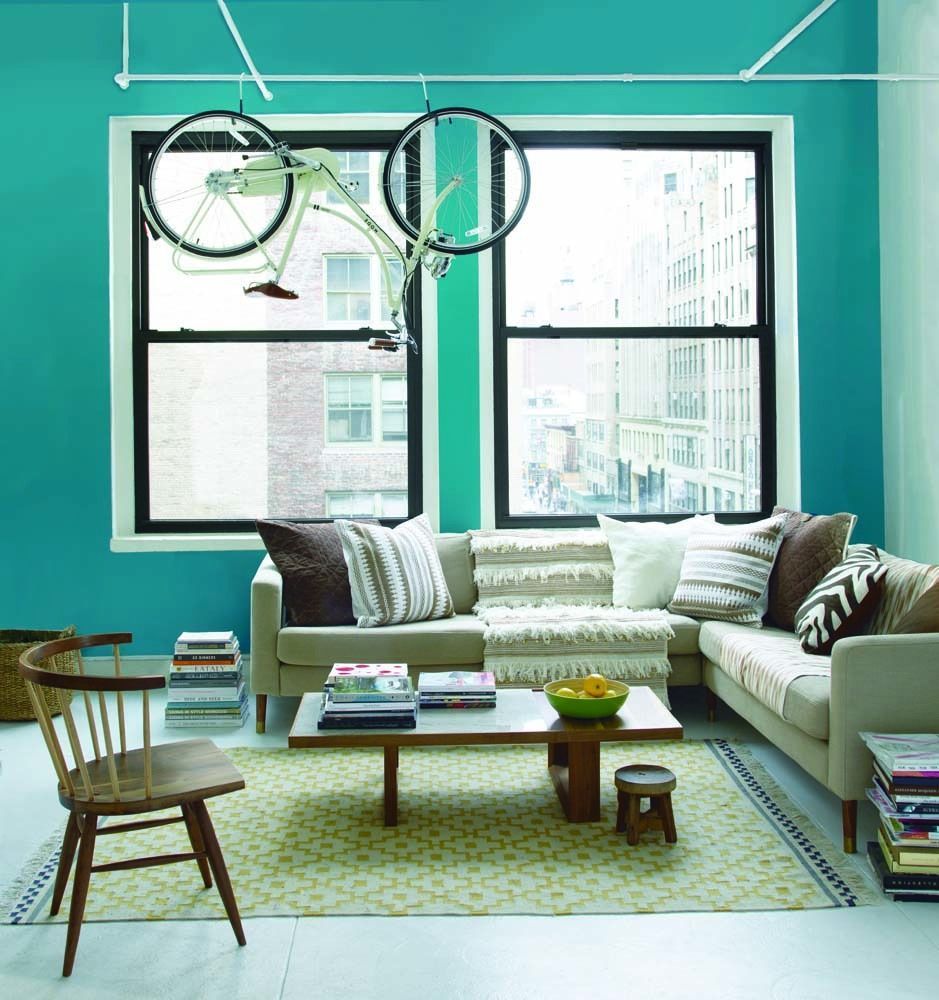 Bright teal living room with a sectional sofa, coffee table, chair, and bicycle hanging by the window.