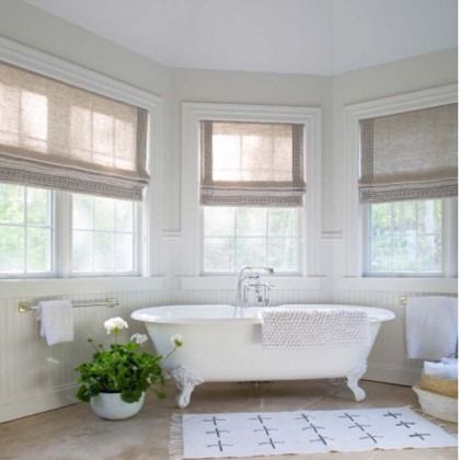 Bright white bathroom with clawfoot tub, windows with shades, and a potted plant on the floor
