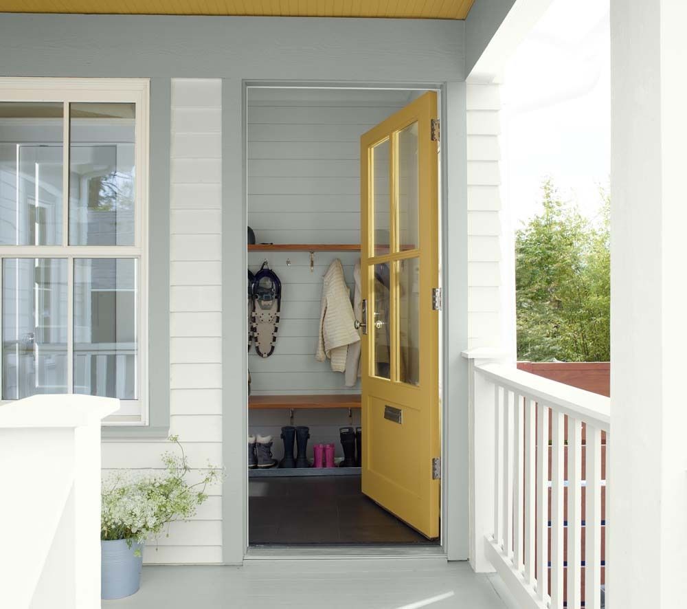 Front porch with open yellow door, white siding, and a small entry nook with hanging coats and shoes.