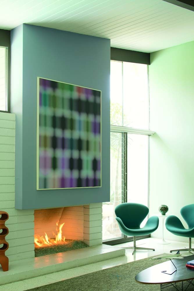 Modern living room with a fireplace, abstract wall art, and green chairs by tall windows