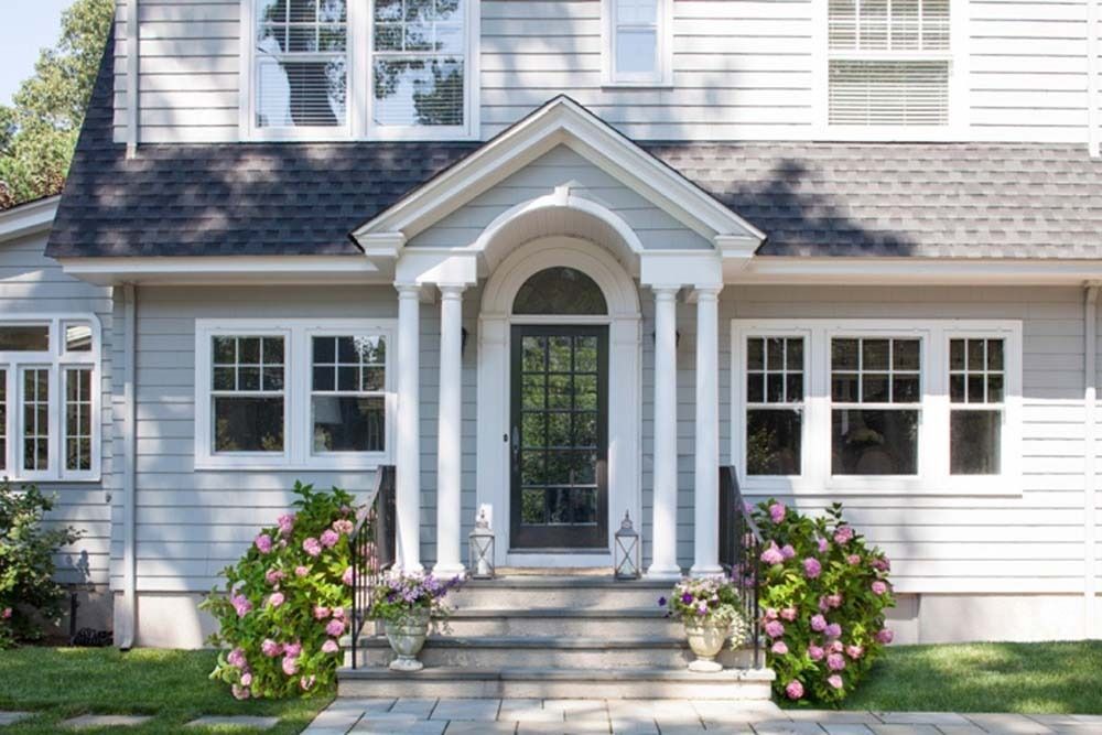 White house front entrance with porch, steps, and pink flowering bushes in front yard