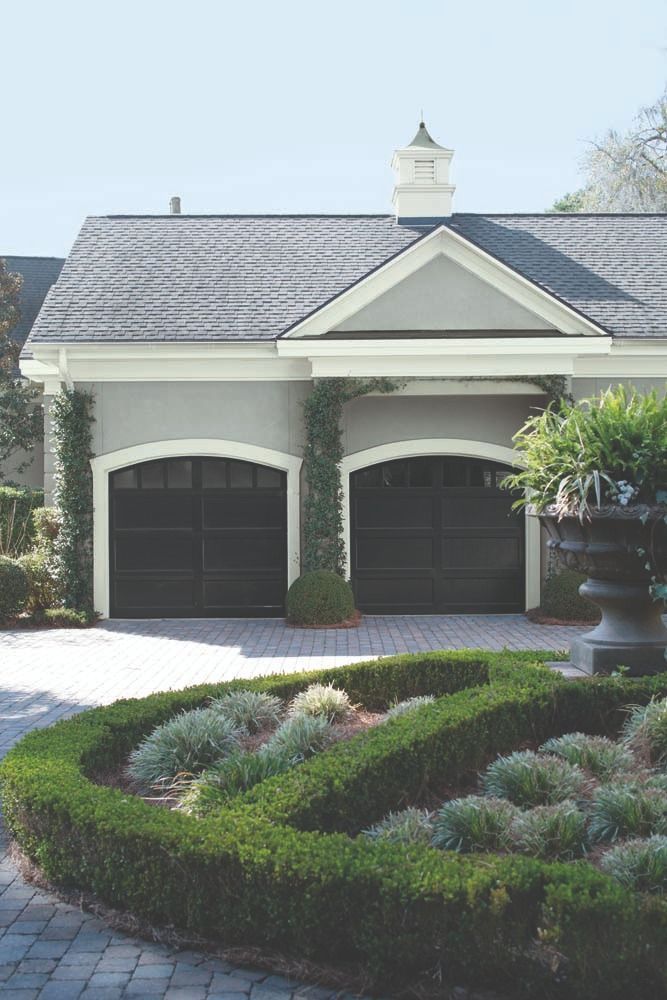 Luxury home exterior with manicured garden, dark garage doors, and a decorative fountain in front