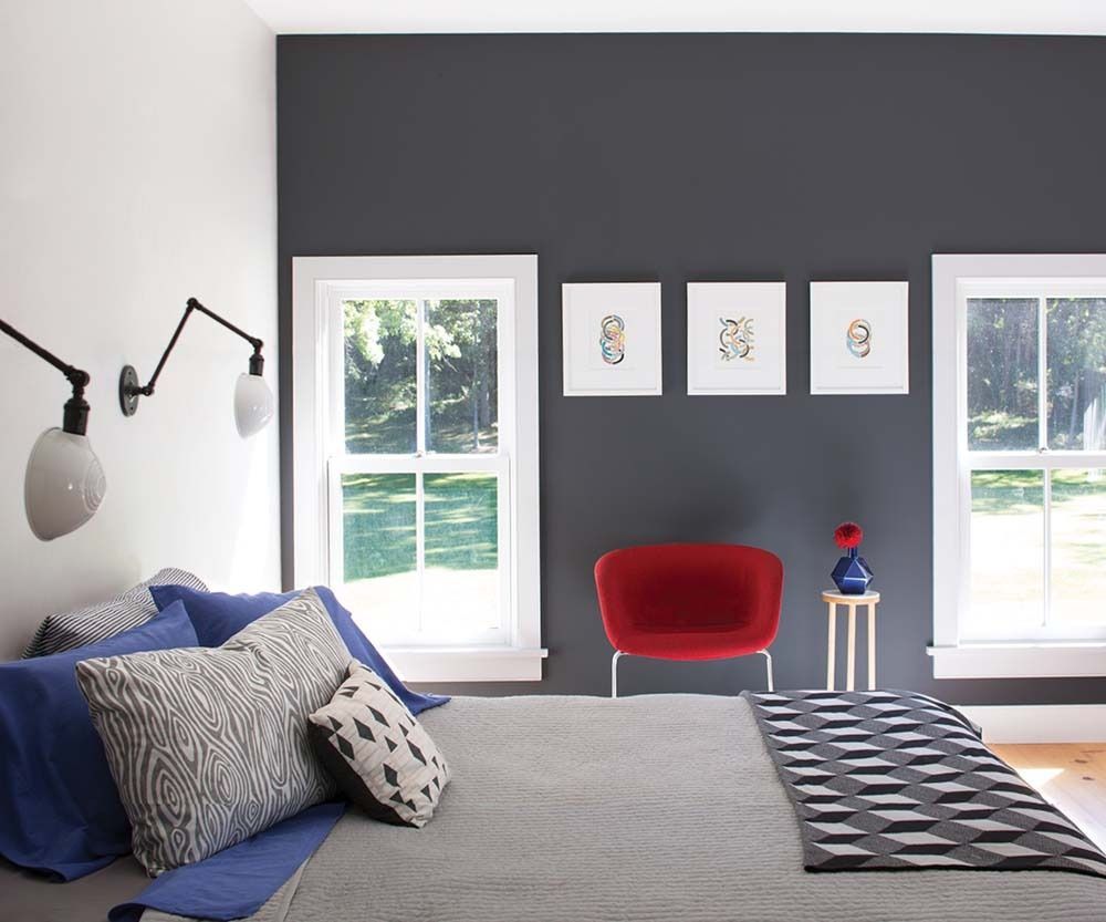 Modern bedroom with gray walls, red chair, blue bedding, and sunlight through two windows