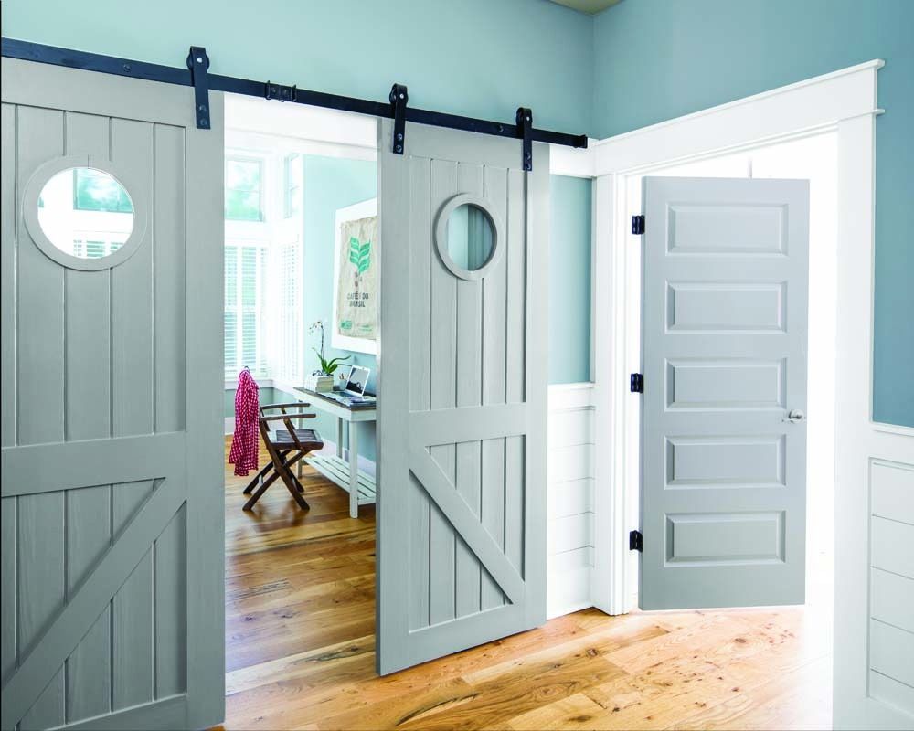Open gray barn doors leading to a bright room with a desk and wooden floor.
