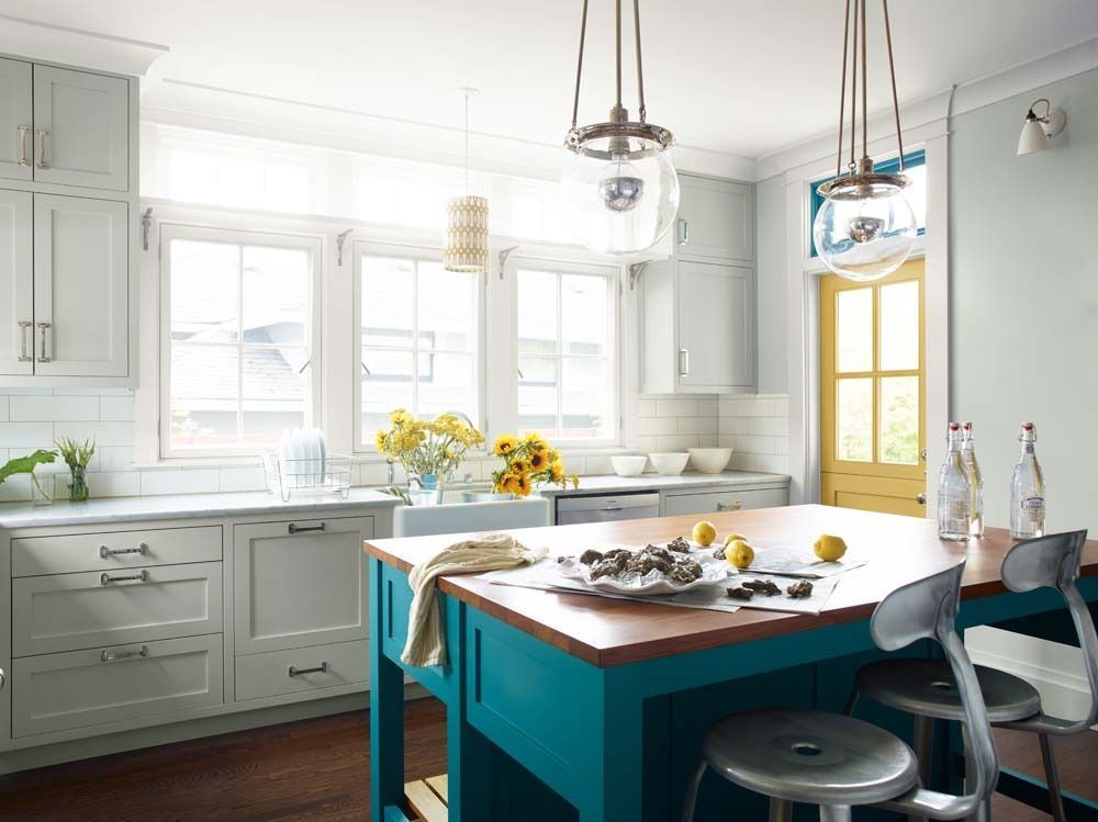 Bright white kitchen with teal island, hanging lights, and a sunlit table with flowers and dishes